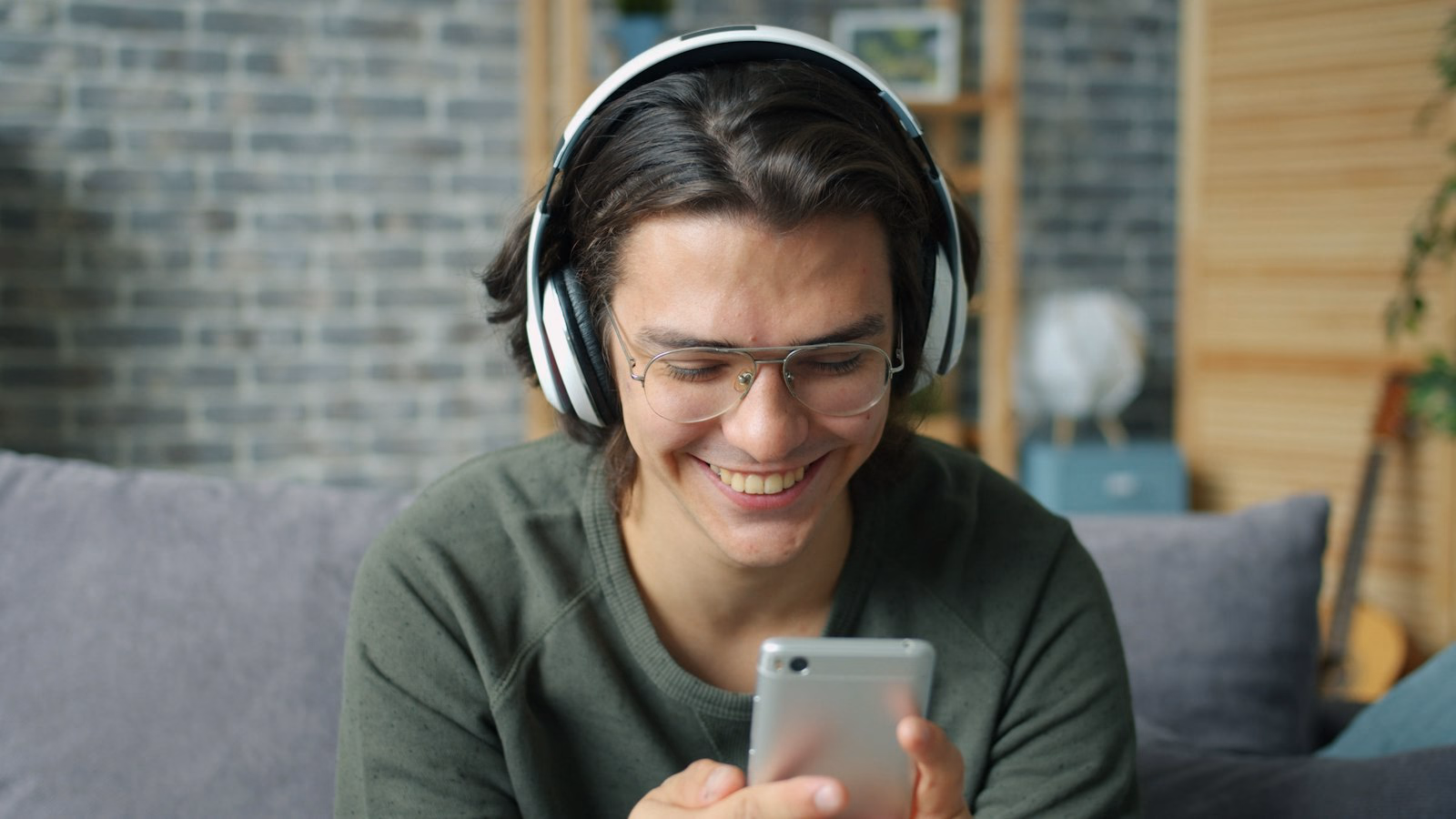 Young man wearing headphones smiling at his phone